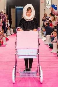 Foto de una modelo de ropa infantil en un desfile con un cochecito rosa de Bebelux